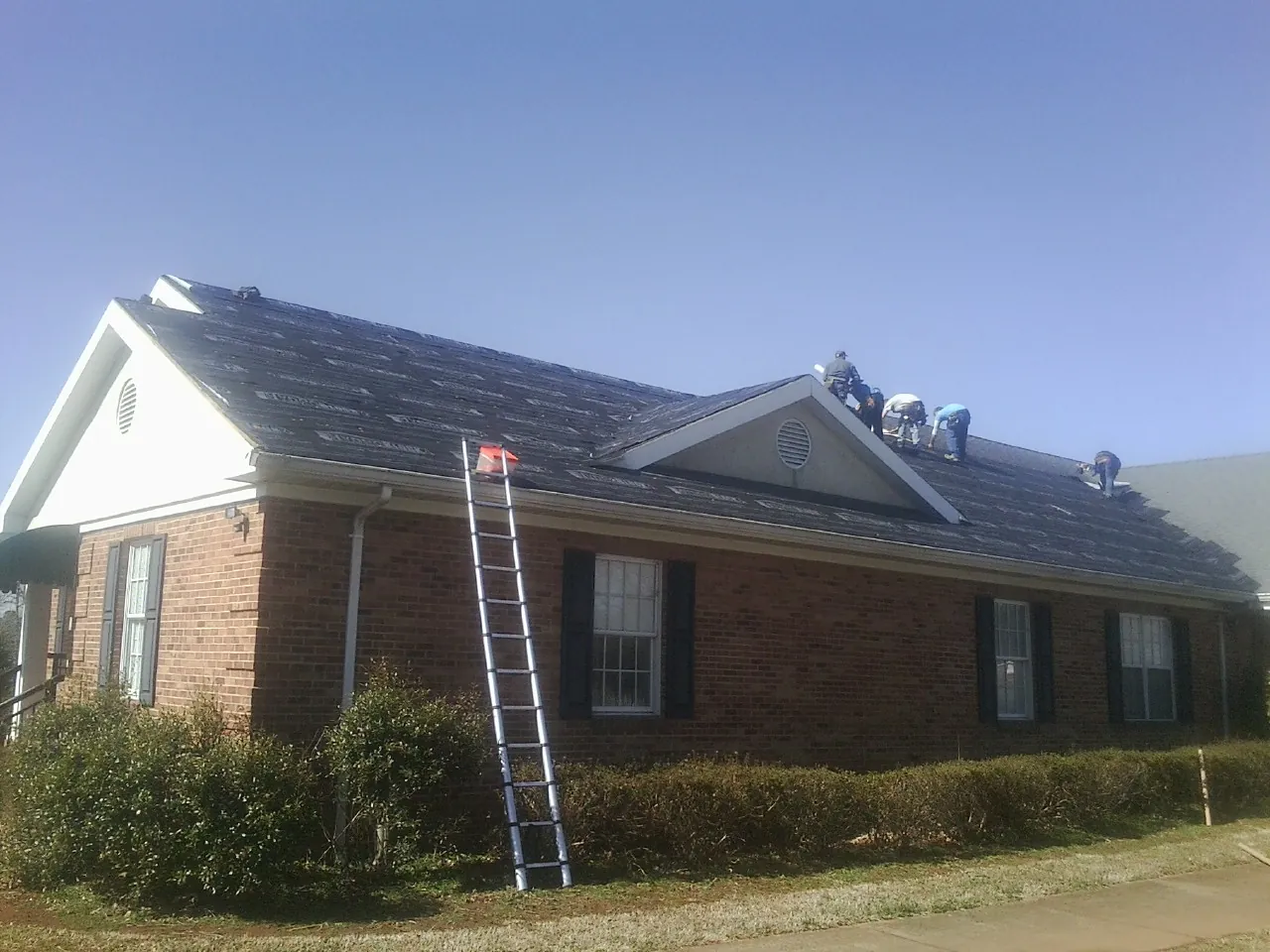 Crew tearing shingles off a brick ranch roof with a ladder set — Emergency Roof Repair work by our crew in Valley Center