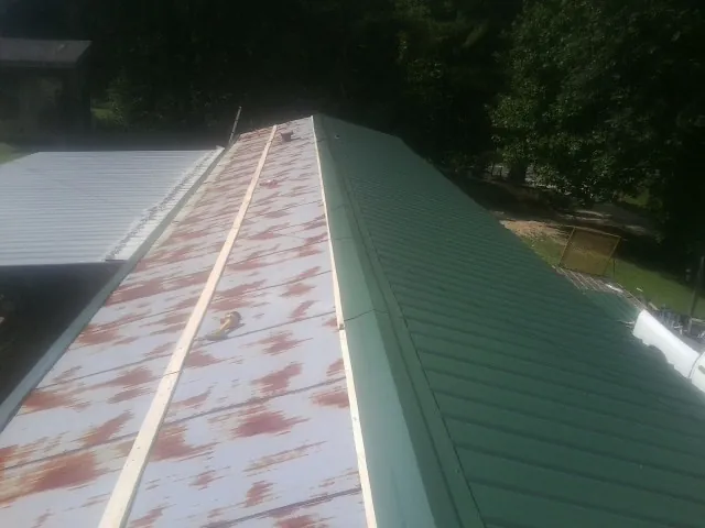 Old rusted panels beside newly installed green metal roofing in Valley Center